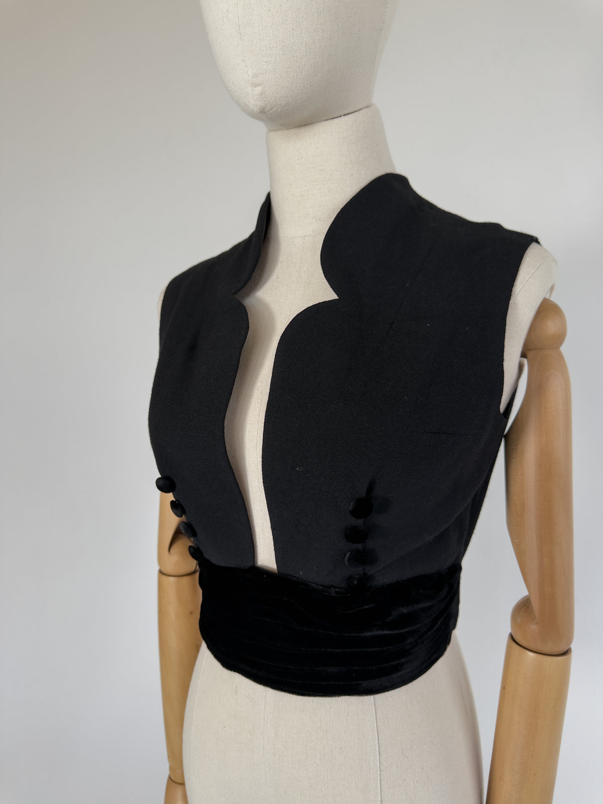 black wool crepe vest with a sculptural notched collar and velvet-covered buttons, over an attached velvet cummerbund, on a dress form