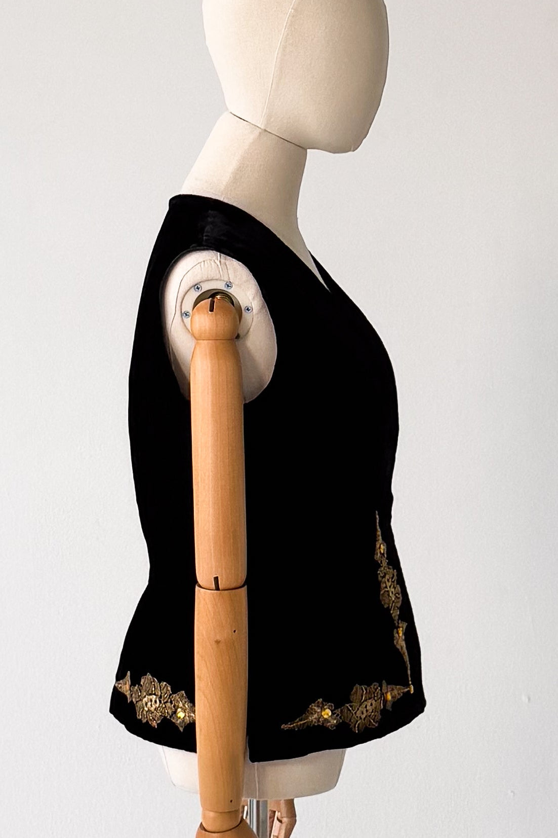 A black sleeveless vest with gold embroidered trim displayed on a mannequin torso against a plain light gray background.