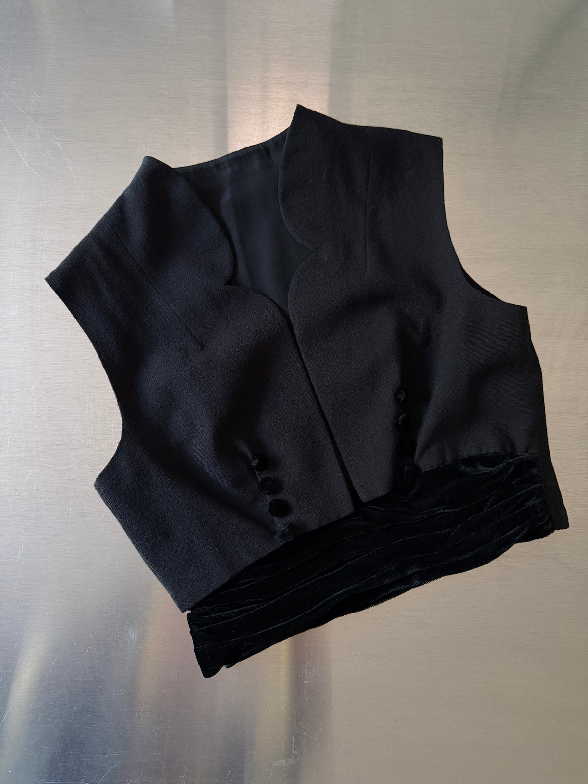black scalloped vest laid flat, front view, showing the notched collar and velvet-covered buttons