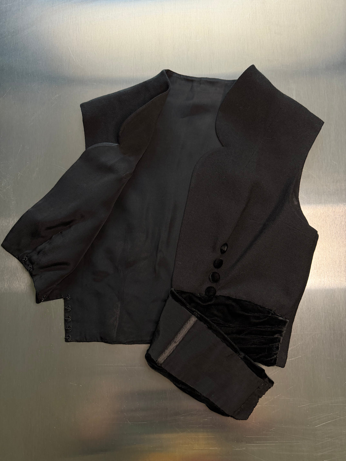 the black scalloped vest turned open, showing the satin-finished interior and hook-and-eye closure