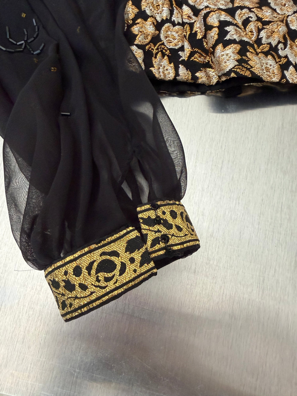 close-up of the sheer sleeve cuffs on the gold brocade blouse, finished with gold scrollwork tape trim