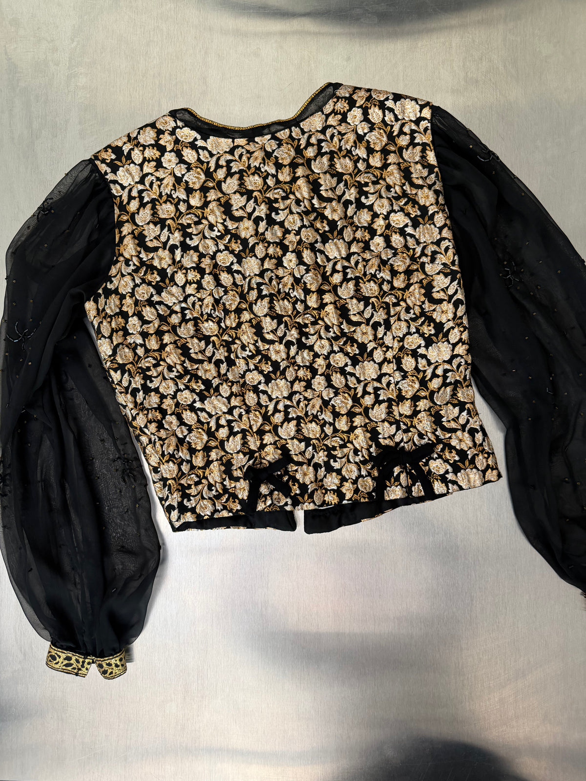gold brocade blouse laid flat, back view, showing small velvet bows at the princess seams