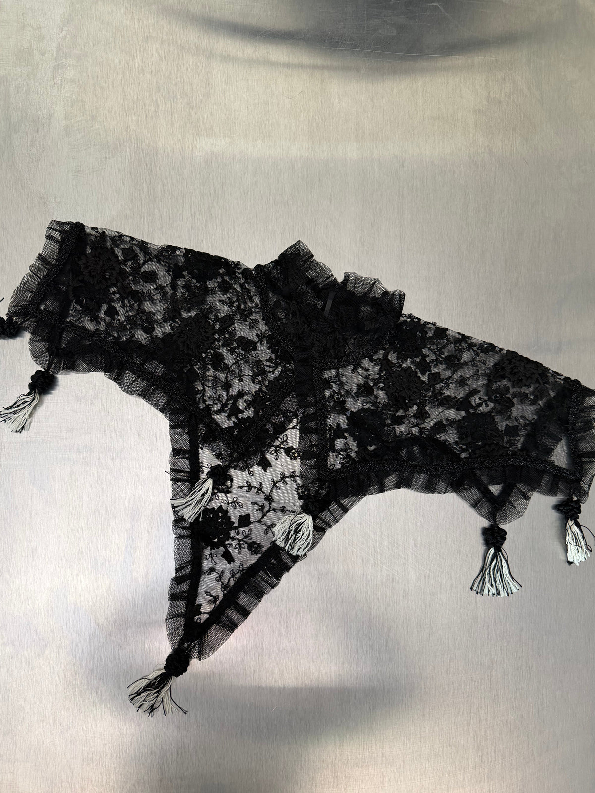 black lace shawl laid flat, showing its full triangular shape with tassel trim at each point