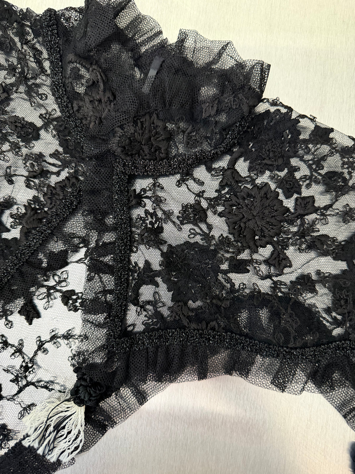 close-up of the black lace shawl, showing the floral lace pattern, ruffled high collar, and tassel trim