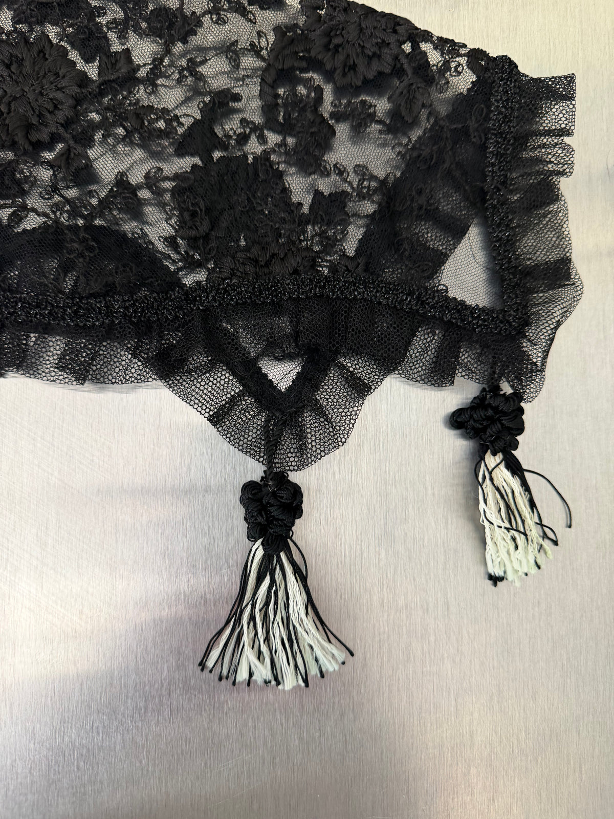 close-up of two black-and-white tassels at the fringed edge of the black lace shawl