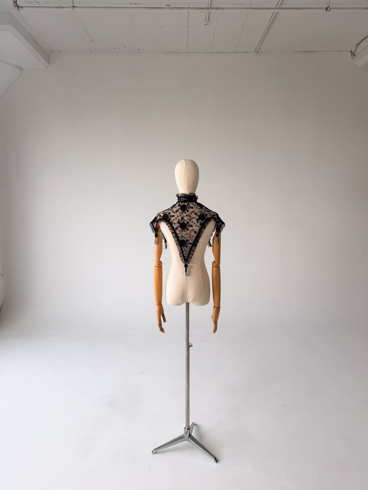 full-length front view of the black lace shawl on a dress form on a tripod stand, showing the pointed drape at the front