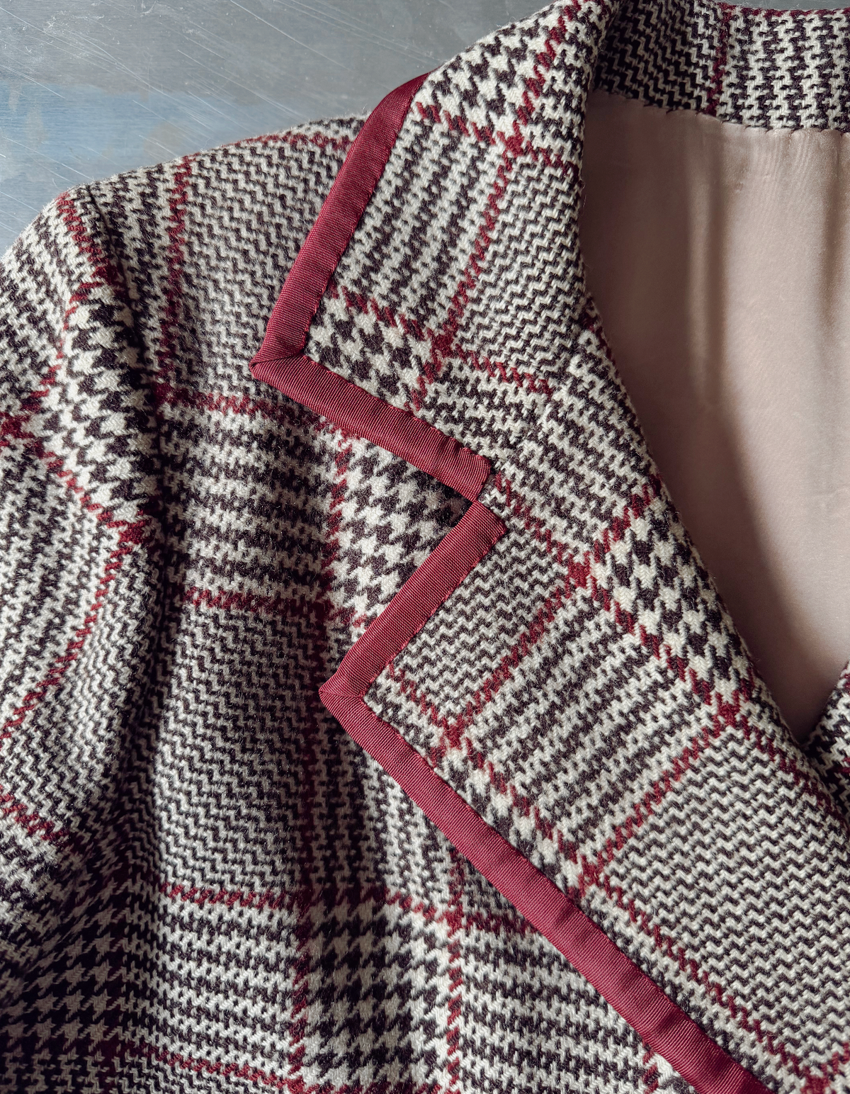 Close-up of a houndstooth blazer with a red and black pattern, featuring a contrasting dusty rose pink quilted lapel trim.
