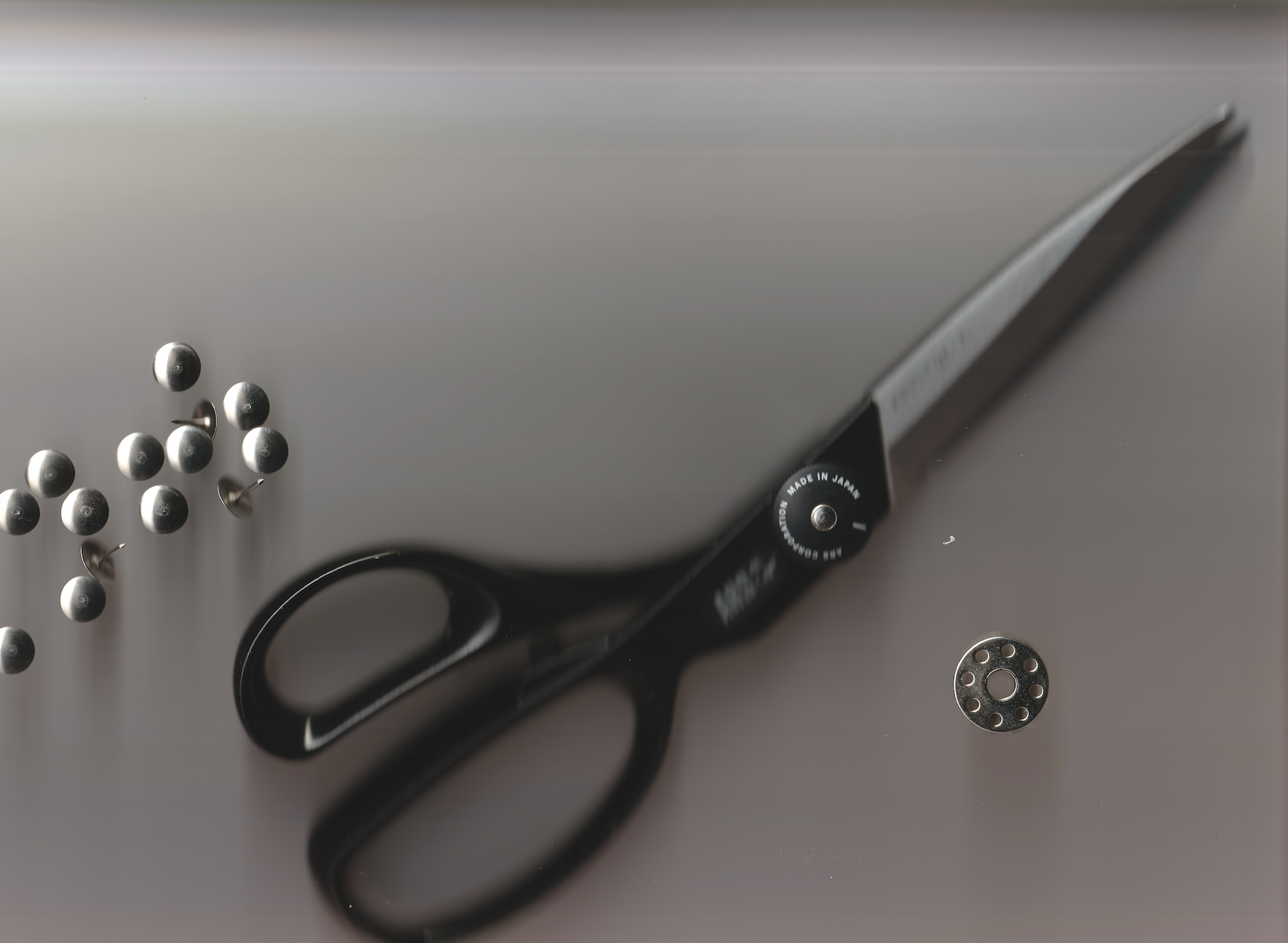 Flat-lay of black tailoring shears, silver pins, and sewing tools against a neutral background, featuring the Other Matters Atelier logo — symbolizing precision, craftsmanship, and intentional design.