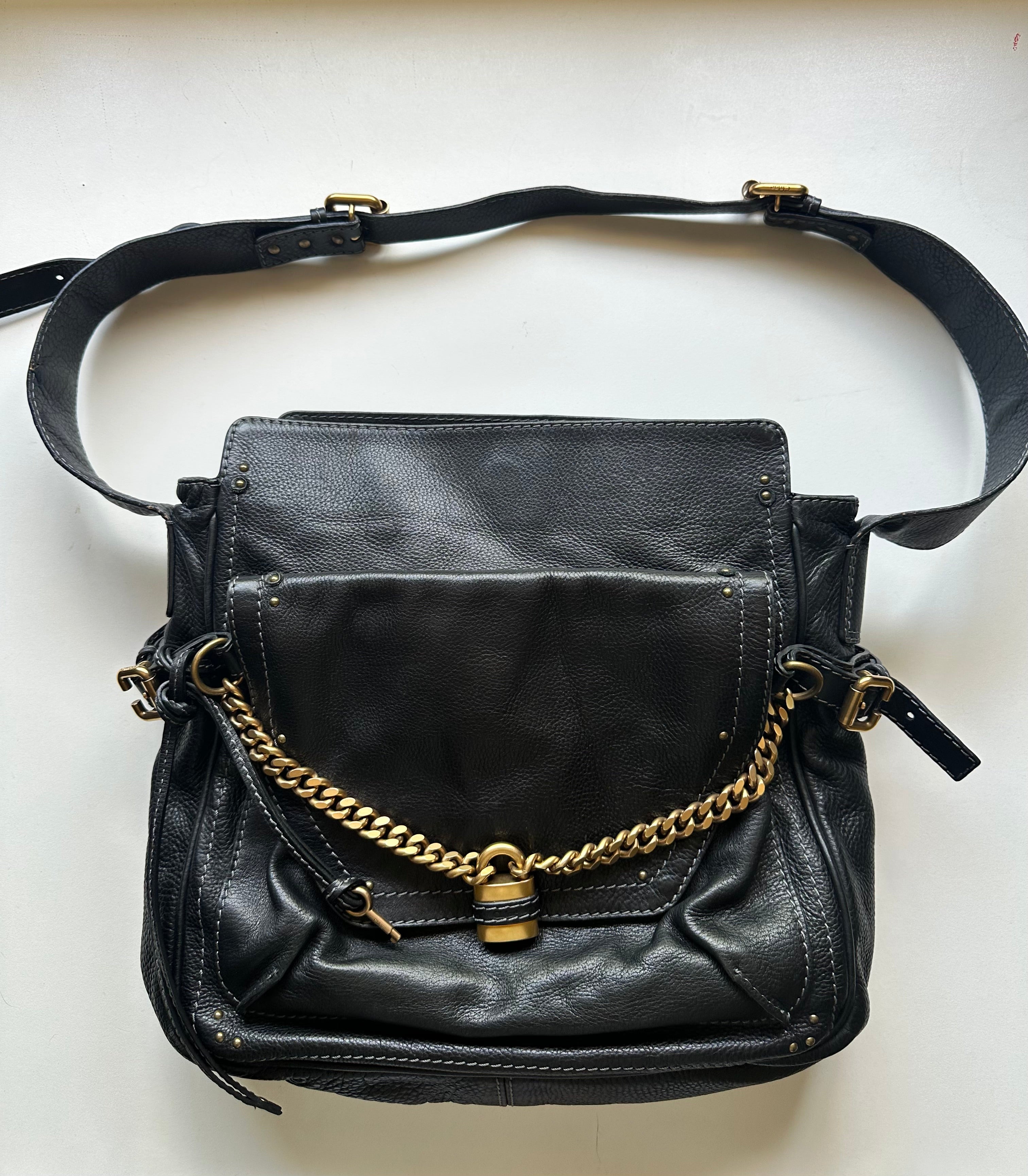 Front view of Chloé Paddington Capsule bag showing gold chain handle, brass padlock closure, and wide detachable crossbody strap, black leather