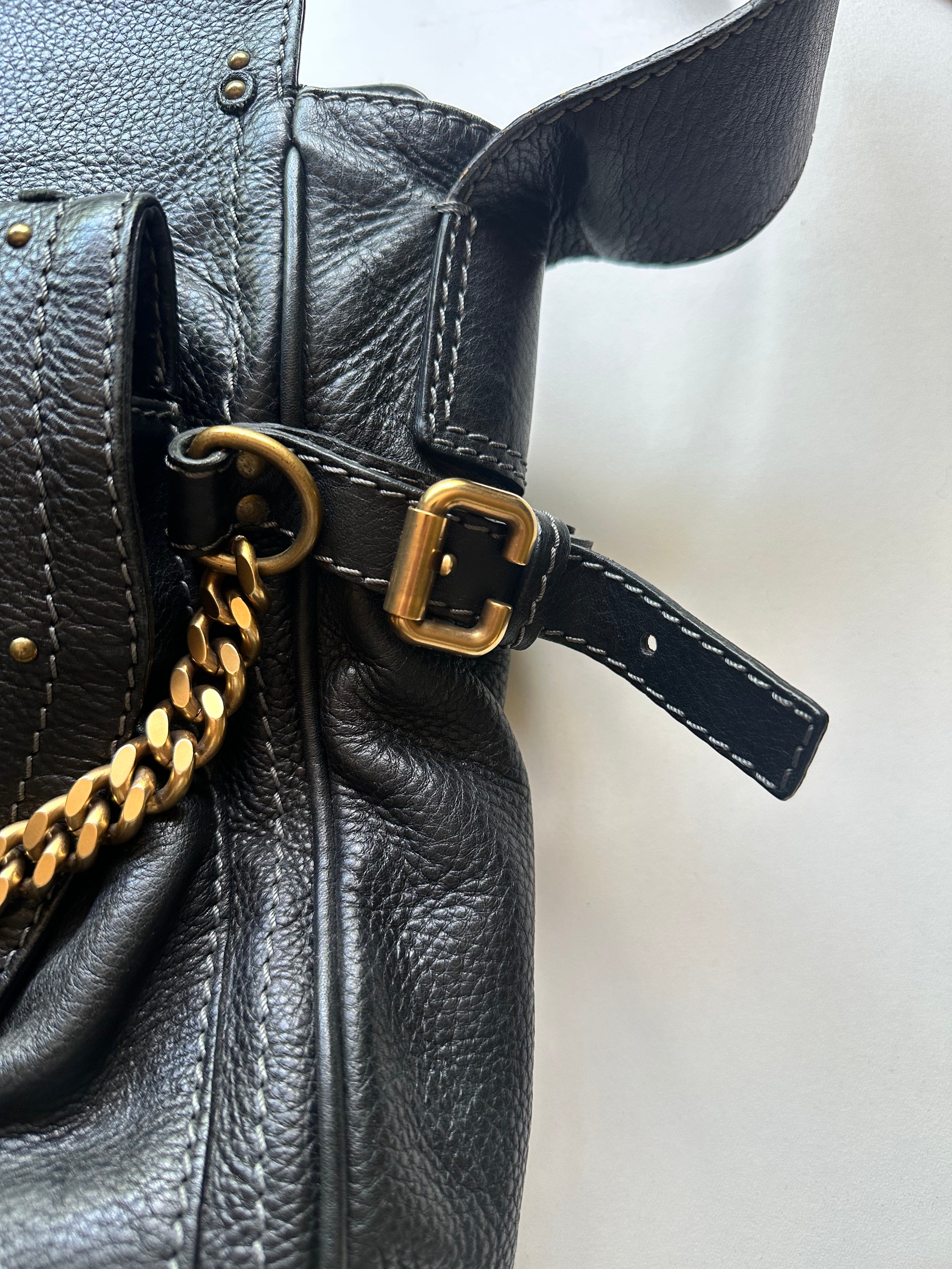 Close-up of brass C-buckle hardware detail on Chloé Paddington Capsule black leather bag, antique gold tone
