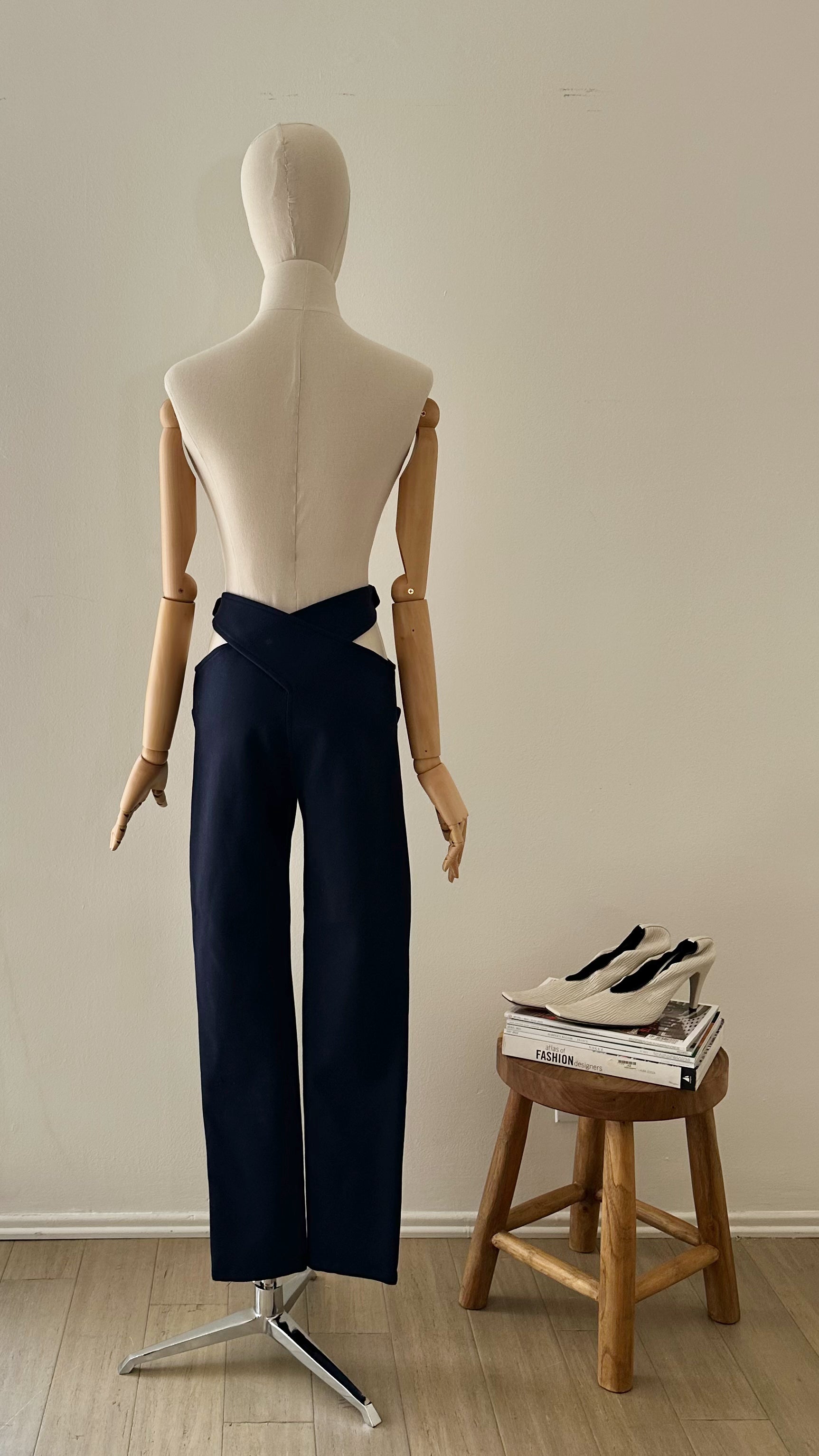 Mannequin wearing navy pants with a wooden stool and books in the background