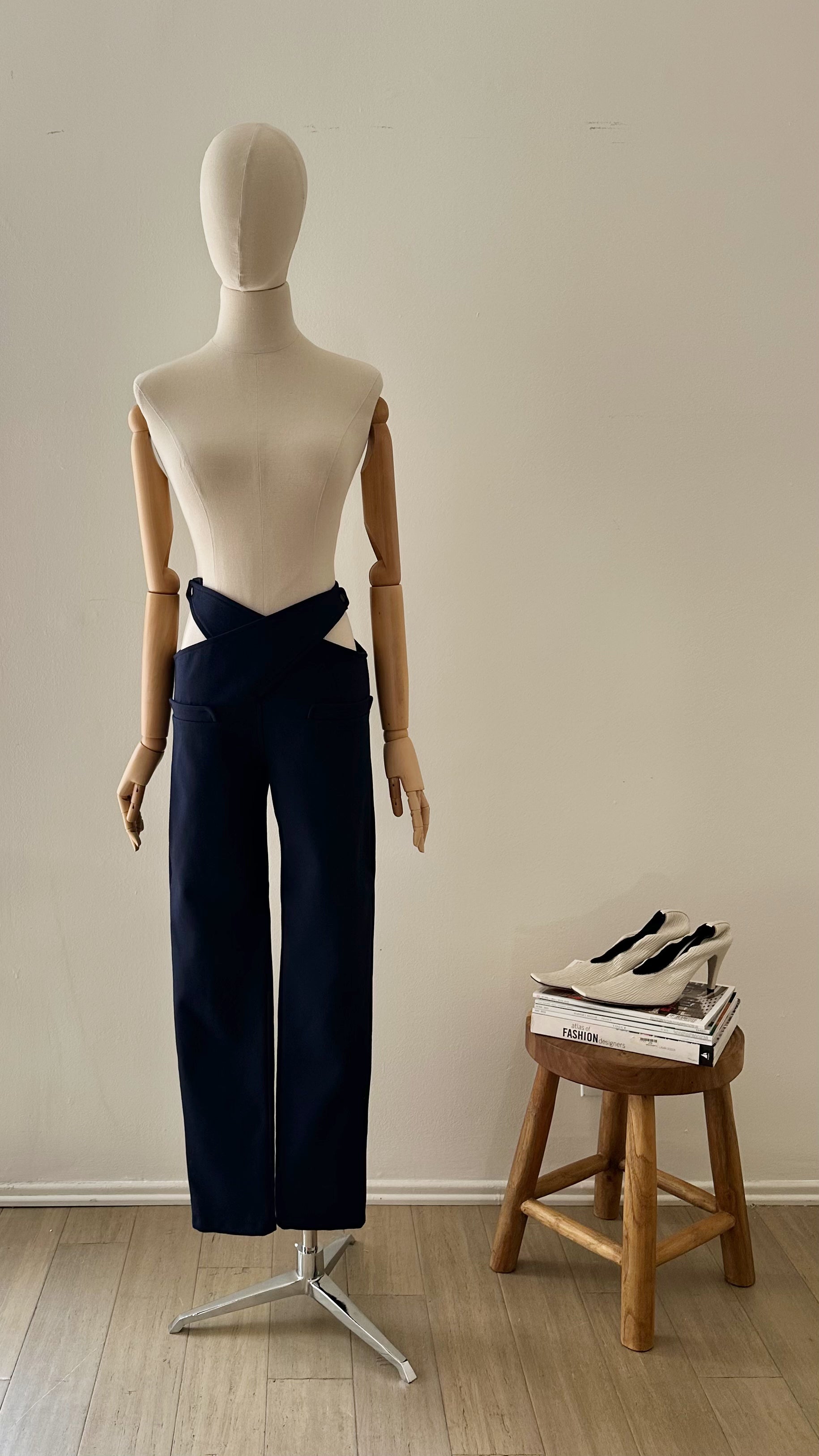 Mannequin wearing navy pants with a wooden stool and shoes in the background