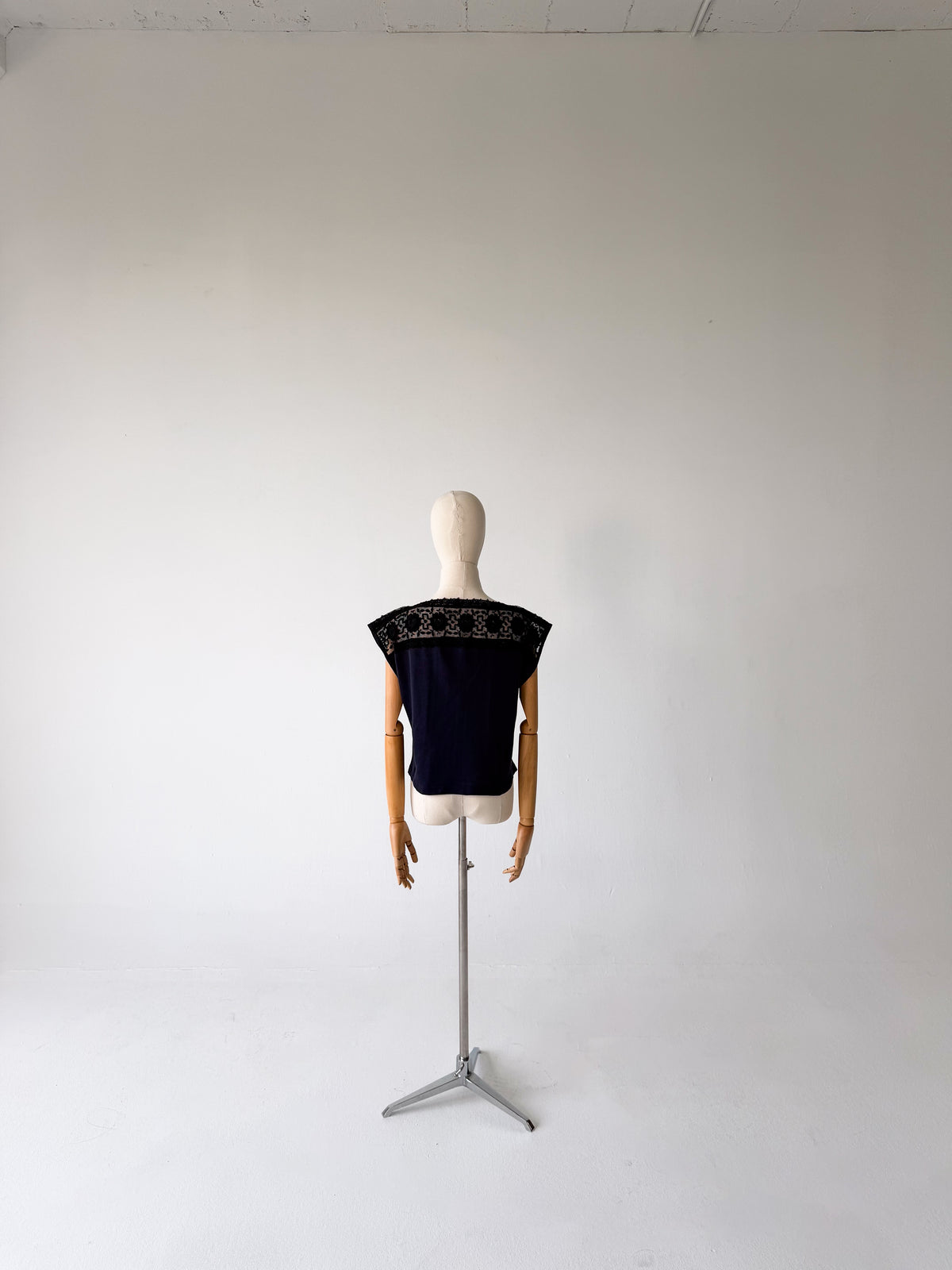 back view of the black jersey top with black lace yoke, on a dress form on a tripod stand against a white backdrop