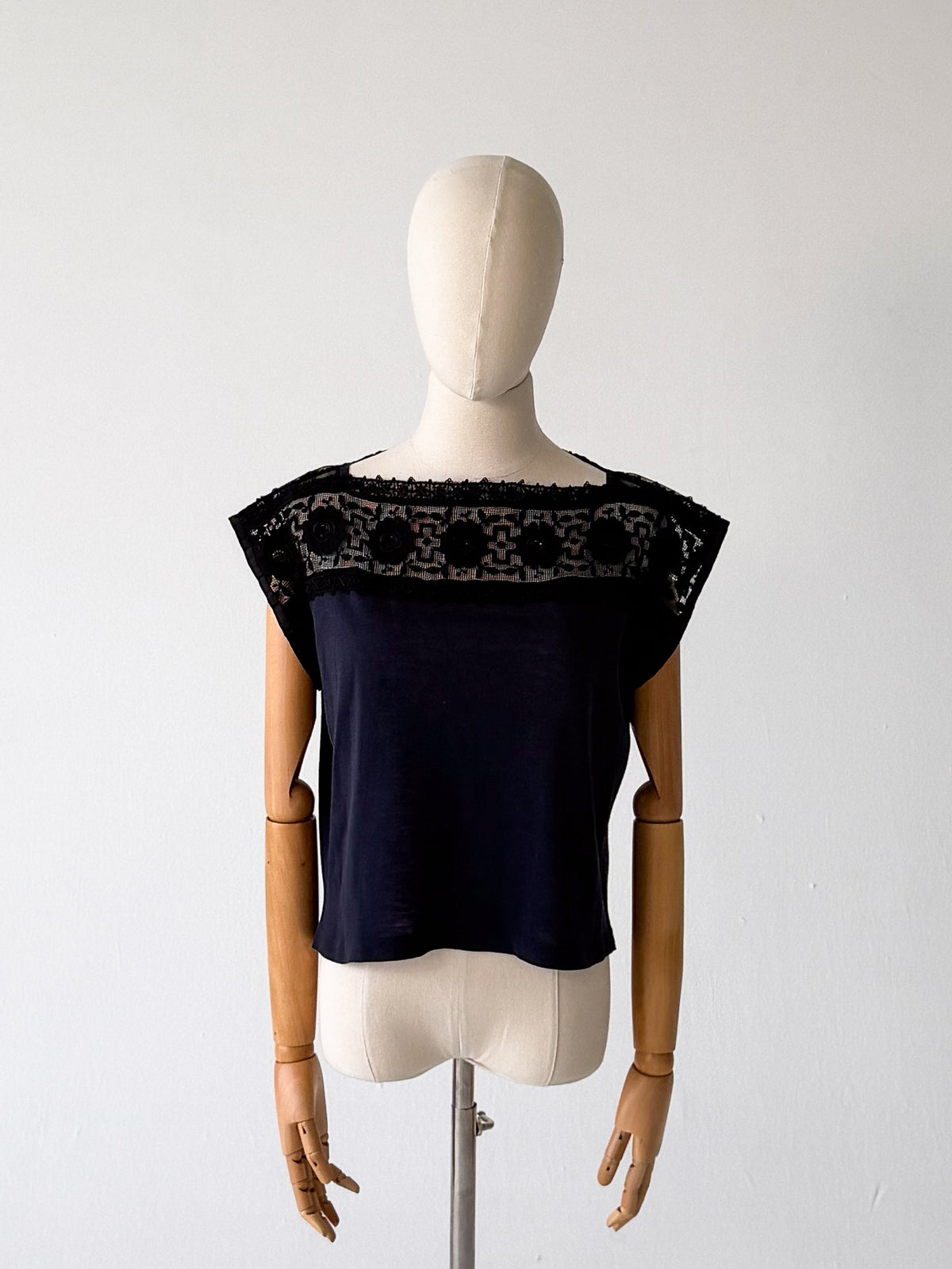 black jersey top with black guipure lace yoke in a floral medallion pattern, cap sleeves, on a dress form against a white studio background