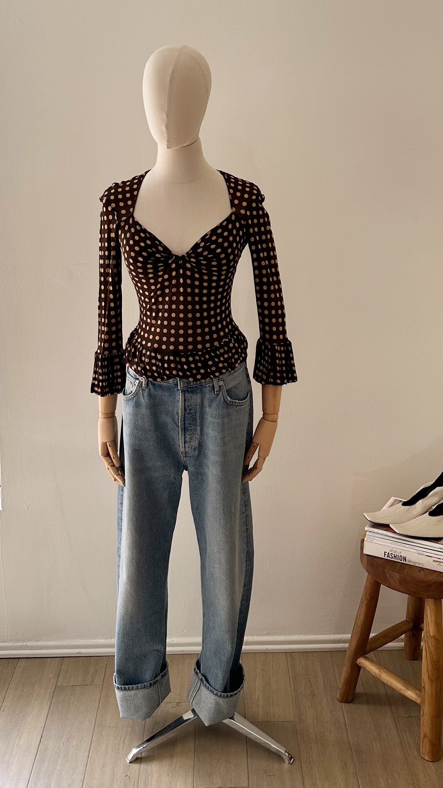 Mannequin wearing a polka dot top and jeans against a plain wall.